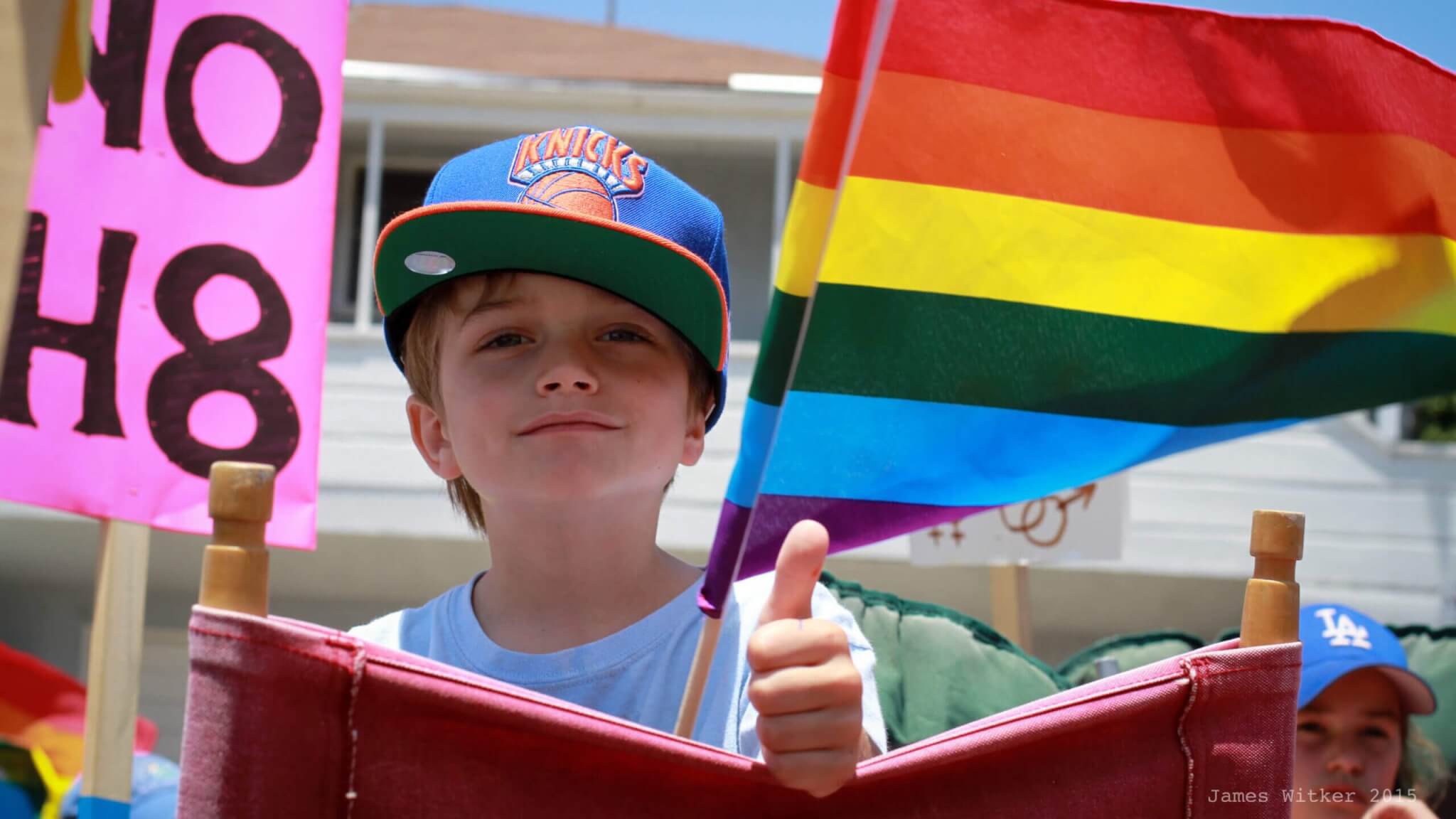 Boy with cap giving thumbs up and pride flag in the background