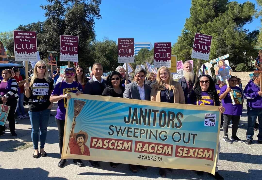 Persons in a demonstration march holding signs that read "CLUE" and a banner reading "Janitors Sweeping Out Fascism Racism Sexism"