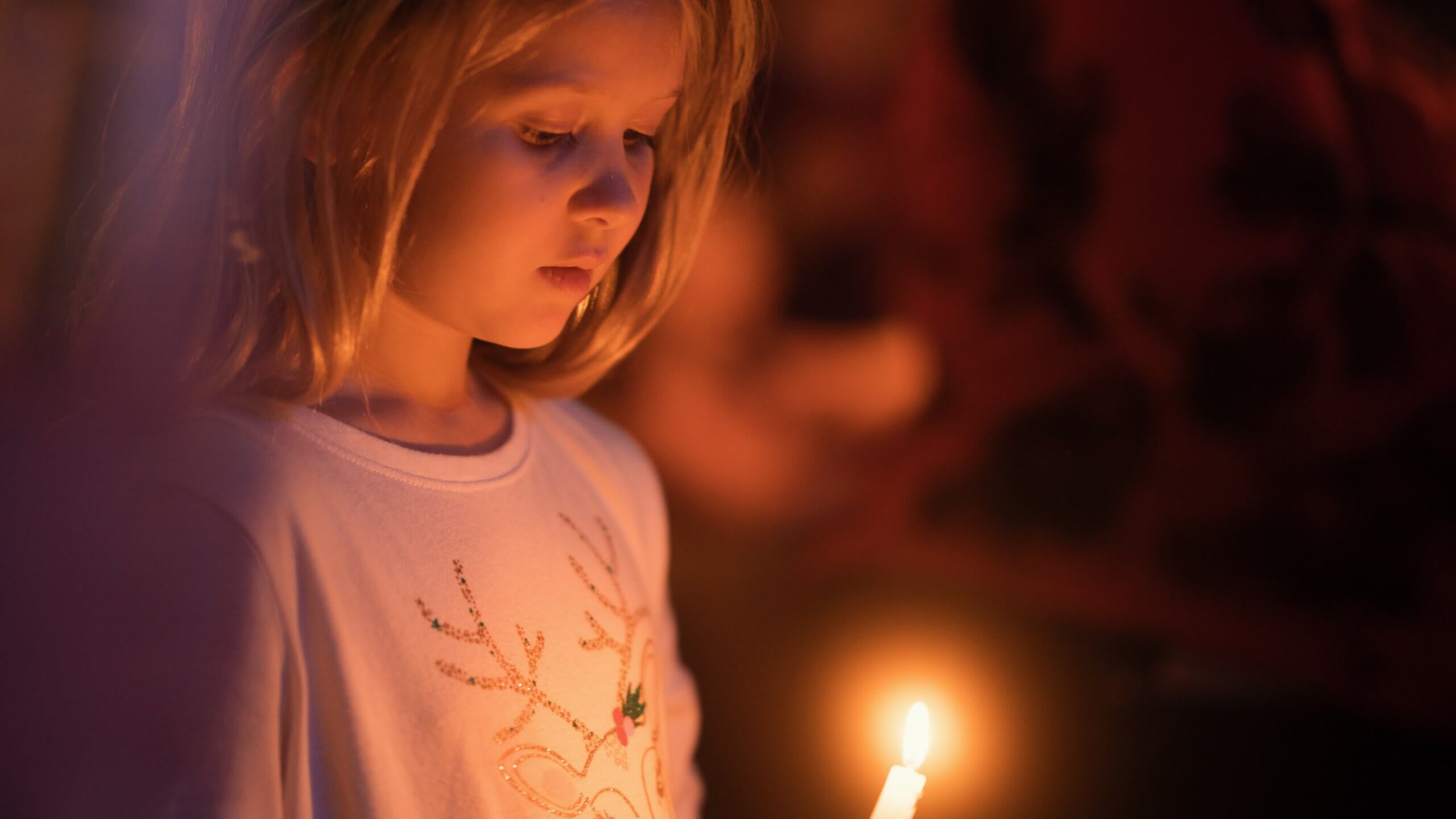 Girl gazes down at a candle she holds - Christmas candlelight service
