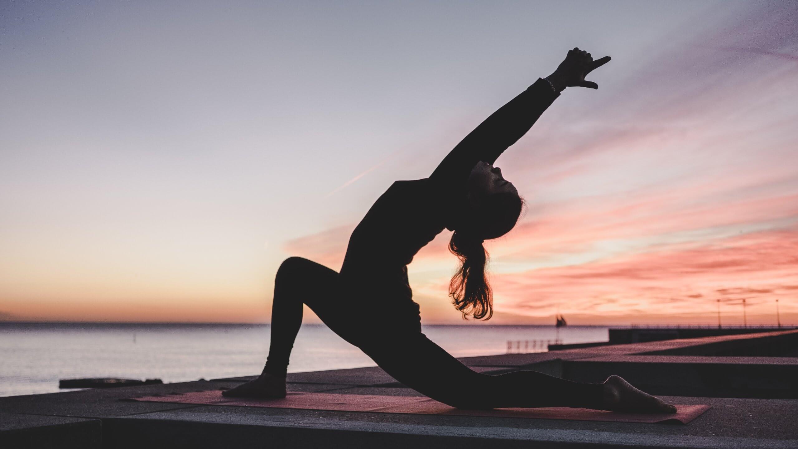 woman at sunrise does yoga pose overlooking water