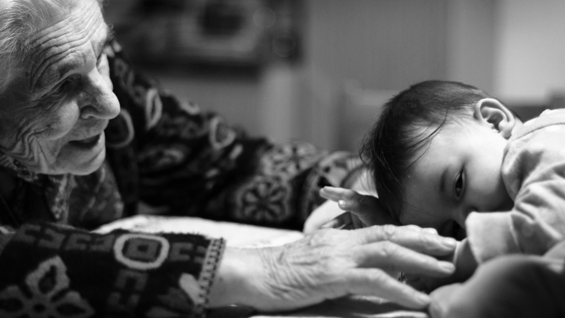 elderly woman reaches toward infant lying down; close up, black and white