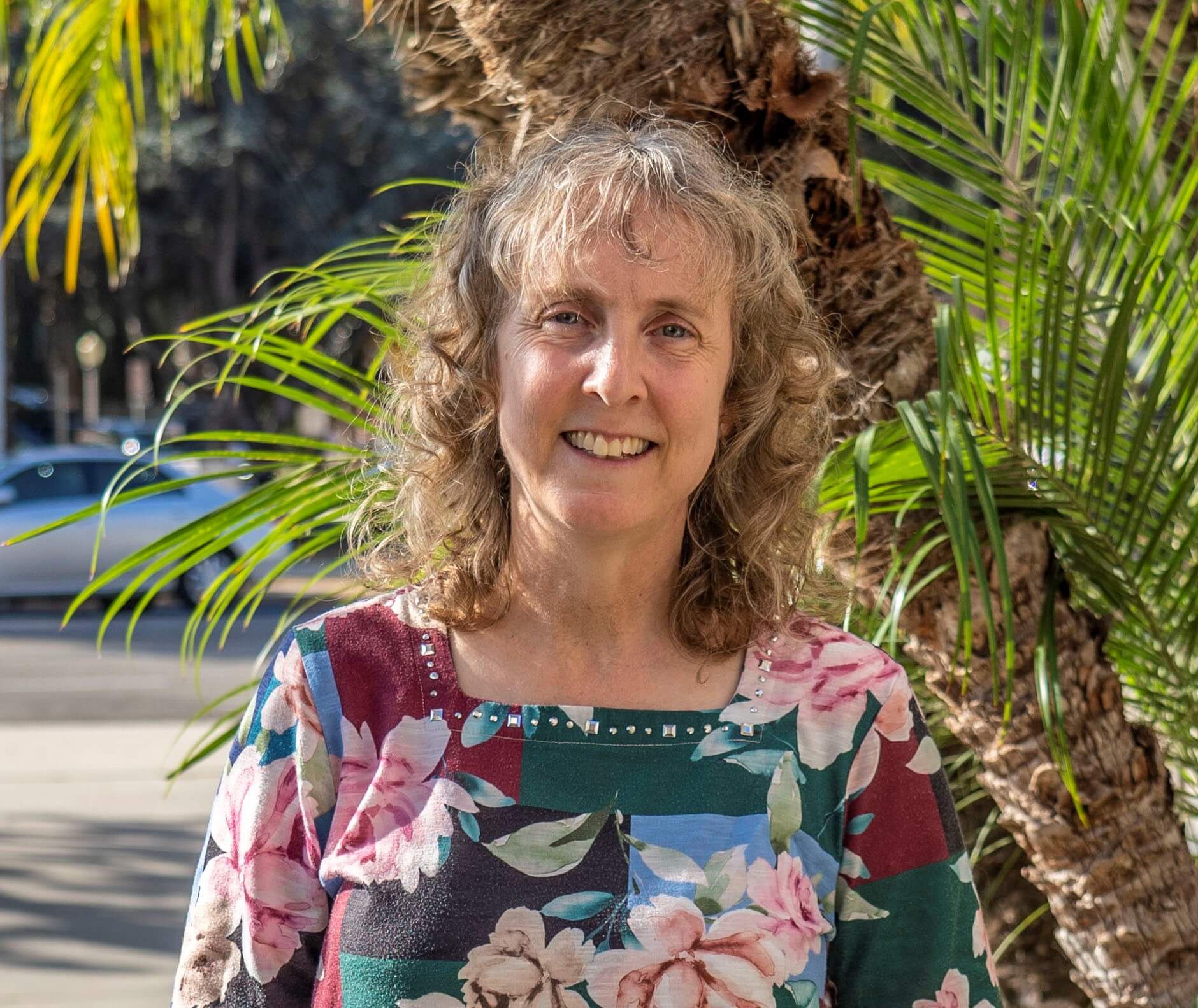Smiling woman with palm trees in background; Sarah Robson - photo