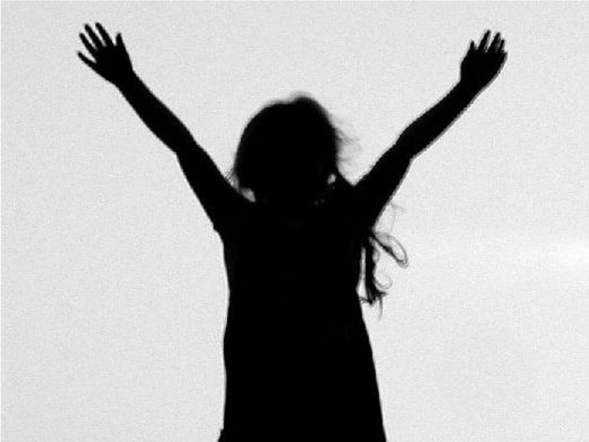 dark silhouette of child with long hair, arms upraised; against gray background - photo