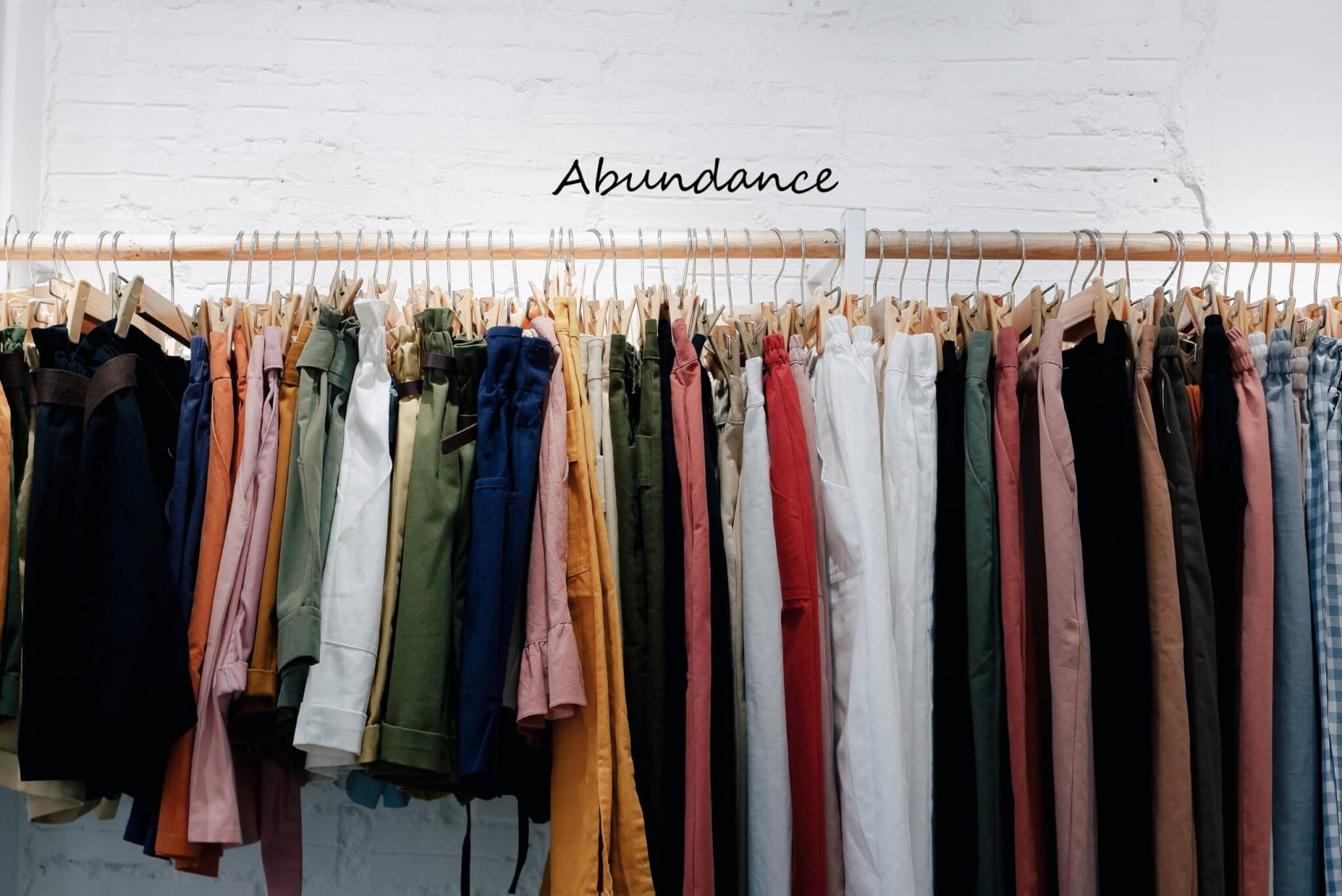 Wall-mounted rod crowded with harngars holding women's pants and shorts; white background with text reading "Abundance" - photo