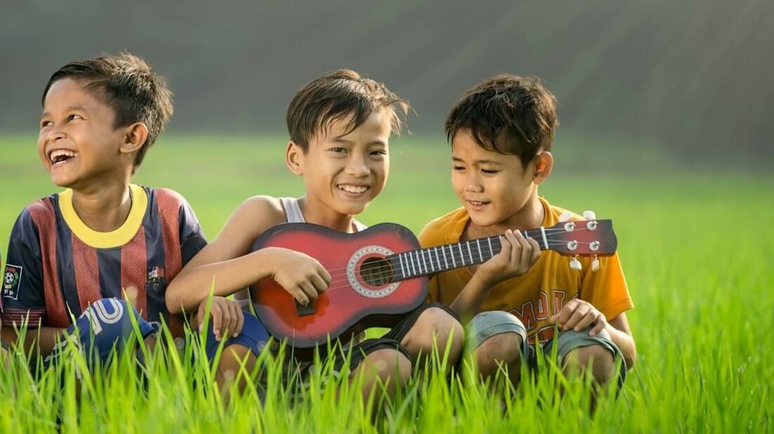 four boys laughing and sitting on grass during daytime