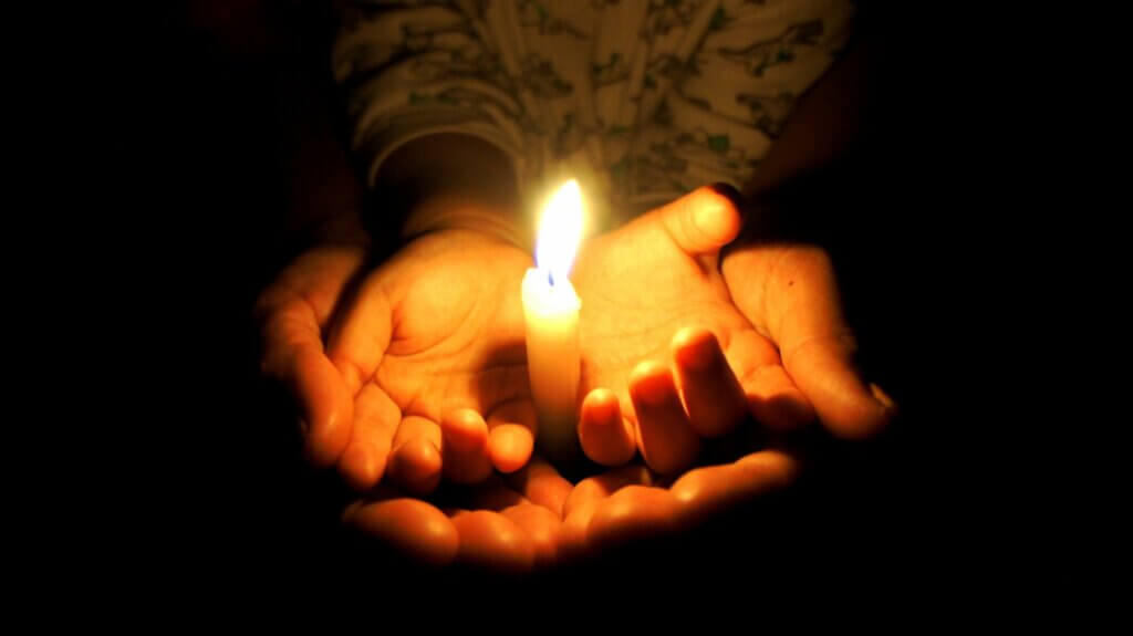 A person holding a lit candle in their hands