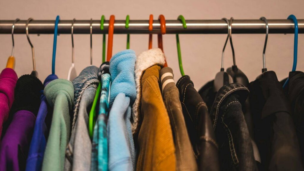 Close-up of various colorful jackets on hangers in a closet setting.