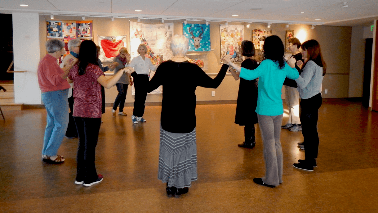 Folk dancers make a circle while learning new steps.