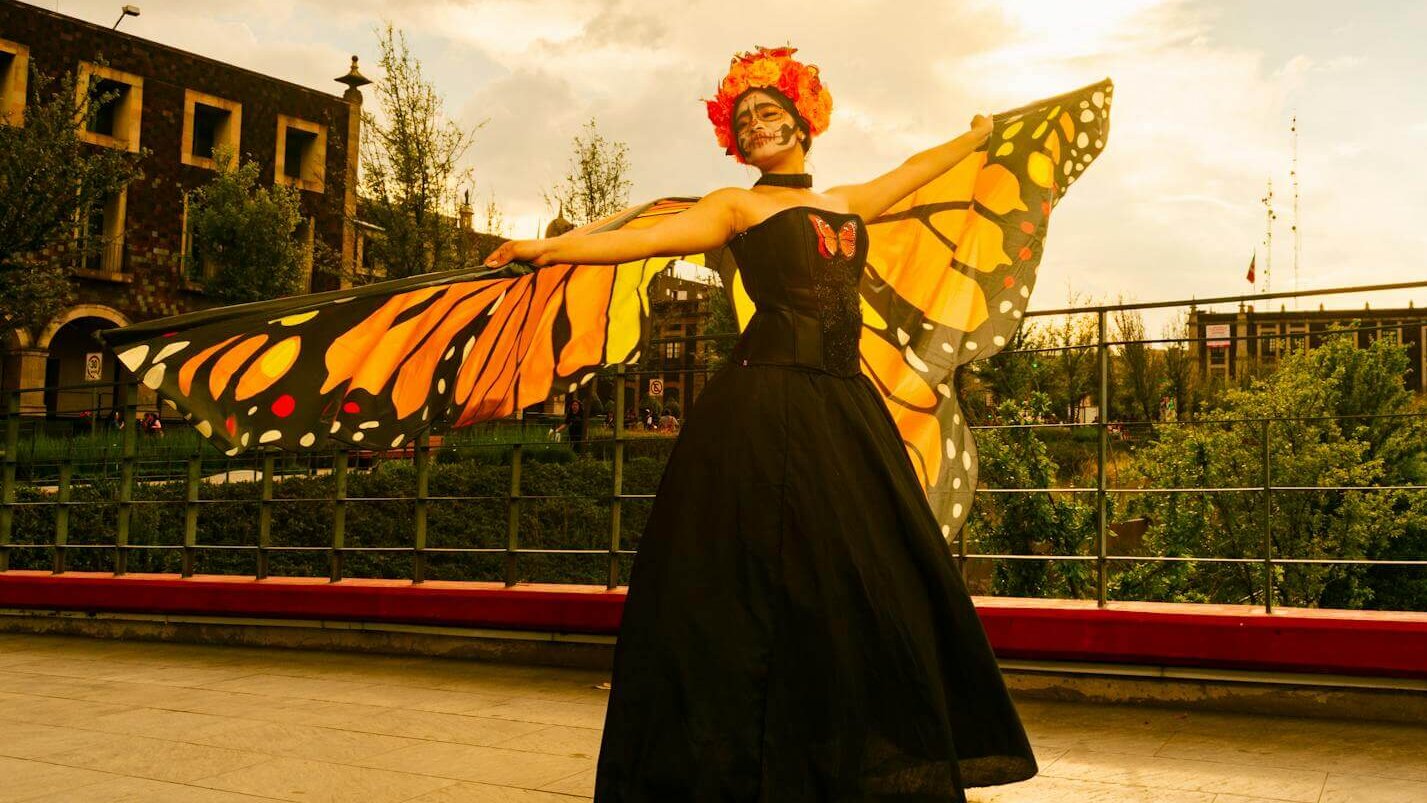 A woman with Day of the Dead makeup in a monarch butterfly costume poses outdoors at sunset in Toluca, Mexico.