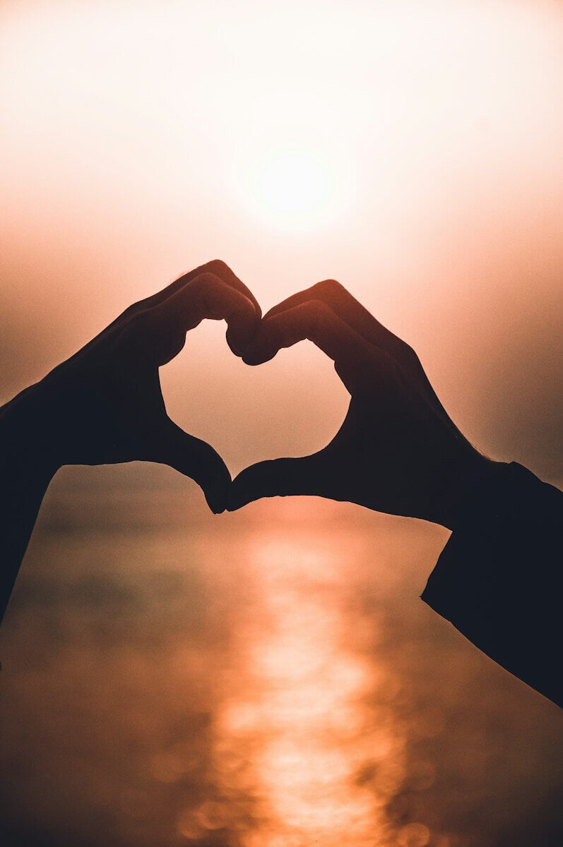 Two hands forming a heart shape silhouette against a warm glowing sky